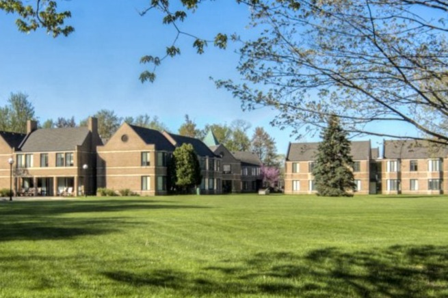 Two brick buildings surrounded by greenery and trees on a clear, sunny day.
